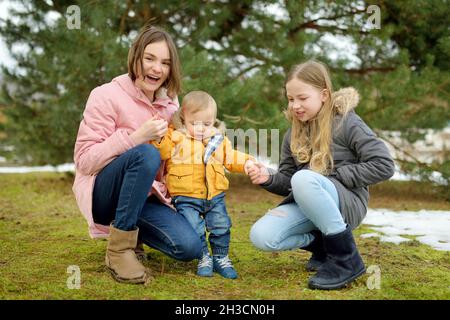 Zwei große Schwestern und ihr kleiner Bruder haben Spaß im Freien. Zwei junge Mädchen halten am Wintertag ihren Geschwisterjungen in der Hand. Kinder mit großer Alterslücke. Kind Stockfoto