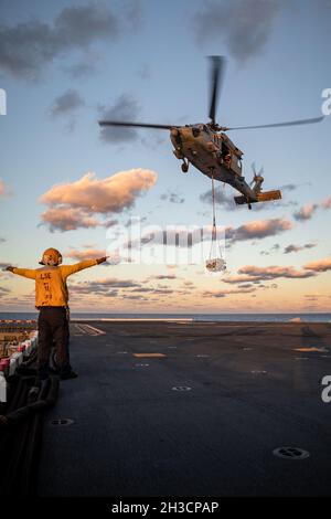 (211026-N-MZ836-1398) ATLANTIK (OKT 26, 2021) Aviation Boatswain's Mate (Handling) 3rd Class Ethan Pendergrass führt einen MH-60S Sea Hawk Hubschrauber, der an das Helicopter Sea Combat Squadron (HSC) 28 befestigt ist, während einer auf Ladung zwischen dem Trocken- und Munitionsschiff USNS Medgar Evers (T-AKE 13) und dem amphibischen Sturmschiff USS Kearsarge der Wasp-Klasse (LHD 3) 26. Oktober 2021. Kearsarge ist dabei, Phibron und Marine Expeditionary Unit Integration (PMINT) zu unterstützen. PMINT bietet die Möglichkeit, mit eingeschifften Marineinfanteristen in einer integrierten Umgebung für amphibische und maritime Operatio zu trainieren Stockfoto