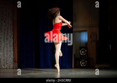 Tänzerin auf der Bühne. Ein Mädchen in einem roten Kleid. Ballerina macht eine Pirouette Stockfoto
