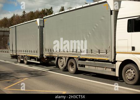 LKW mit grauer Karosserie und weißer Kabine. LKW auf der Straße. Fahren auf der Autobahn. Frachttransport. Stockfoto