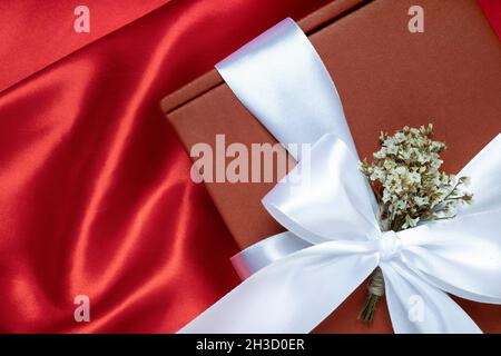 Nahaufnahme einer Geschenkschachtel in Chhristmas- oder Neujahrsrot mit weißem Band und winzigen getrockneten Blumen. Stockfoto