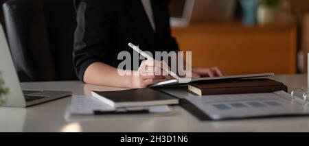 Nahaufnahme der Frau mit Stylus Pen Schreiben auf dem digitalen Tablet, berühren auf dem digitalen Tablet-Bildschirm arbeiten auf Laptop-Computer im Büro Stockfoto