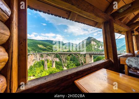 Gesehen durch eine glaslose Öffnung in einem holzgebauten Cafe, mit Blick auf die tiefe Schlucht und den Fluss unten mit wunderschönem Blick auf die Berge. Stockfoto