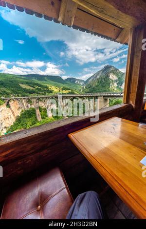 Gesehen durch eine glaslose Öffnung in einem holzgebauten Cafe, mit Blick auf die tiefe Schlucht und den Fluss unten mit wunderschönem Blick auf die Berge. Stockfoto