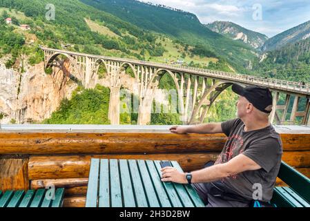 Der Reisefotograf ruht in einem Blockhütten-Café, mit Blick auf die tiefe Schlucht und den Fluss unten mit herrlichem Panoramablick. Stockfoto