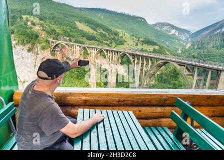 Der Reisefotograf ruht im frühen Herbst in einem Blockhütten-Café, mit Blick auf die tiefe Schlucht und den Fluss unten mit herrlichem Panoramablick. Stockfoto