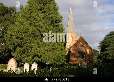 Church of St. John, die kurz nach Sonnenaufgang orange leuchtet, mit Friedhof und Bäumen in Reid, Canberra, ACT, Australien Stockfoto