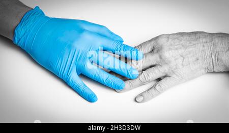 Die Hände des Arztes in blauen Handschuhen halten die Hände einer älteren Frau, einer Patientin. Stockfoto