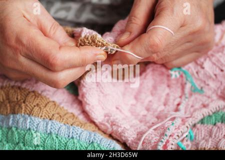 Weibliche ältere Hände mit Falten. Die altersgealterten Hände einer Frau mit Stricknadeln stricken ein Produkt, die Hobbykleidung der Großmutter werden von Hand hergestellt Stockfoto