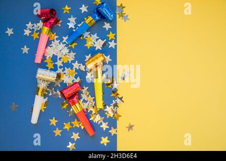 Farbenfrohes Feierstuster mit Party-Gebläsehörnern. Minimales Partykonzept. Flaches Lay.Whistle Gebläse isoliert auf gelbblauem Hintergrund. Speicherplatz kopieren Stockfoto