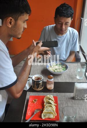 Zwei männliche Freunde genießen Fast Food im Café und machen Fotos von Essen mit dem Handy Stockfoto