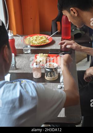 Zwei junge Jungs essen tibetisches Essen im Fast-Food-Café mit dem Smartphone Stockfoto