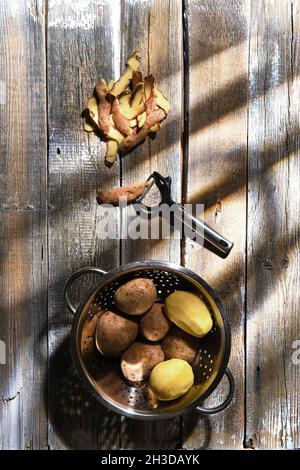 Draufsicht auf frische Kartoffeln und Kartoffelschälungen mit einem Messer auf einem Tisch Stockfoto