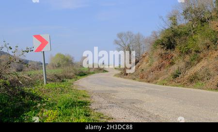 Schotterstraße und herrliche grüne Gras in der Nähe der Straße mit bewölktem und offenen Himmel Hintergrund. Straßenschild neben der Straße. Stockfoto