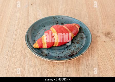 Rotes Frühstückscroissant auf blauem Teller und Holztisch Stockfoto