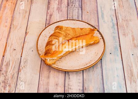 Buttercroissant gefüllt mit geräuchertem norwegischen Lachs und Frischkäse auf einem Porzellanteller Stockfoto