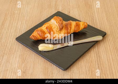 Croissant zum Frühstück mit einem Buttermesser auf schwarzem Teller Stockfoto