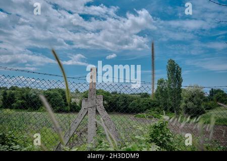 Sperrzone Zäune aus Metall und Stachelband und Betonpfosten mit rundem grünen Gras und Grenzlinie für verlassene und Brachfeld-Zone. Stockfoto