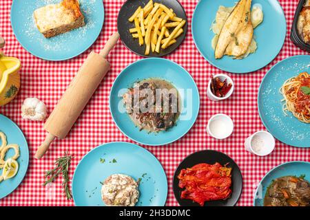 Bild von oben: Mediterrane Gerichte, geröstete rote Paprika, geschmorte Kalbsschienen, Lasagne, gegrillter Seehecht, Spaghetti, russischer Salat und Gewürze Stockfoto