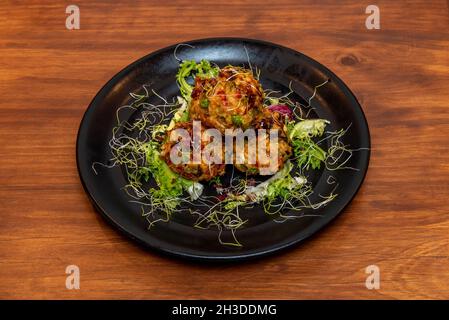 Asiatisches Rezept mit gewürzten Schweinebällchen in Tempura-Teig mit Salat und Bohnensprossen auf schwarzem Teller Stockfoto