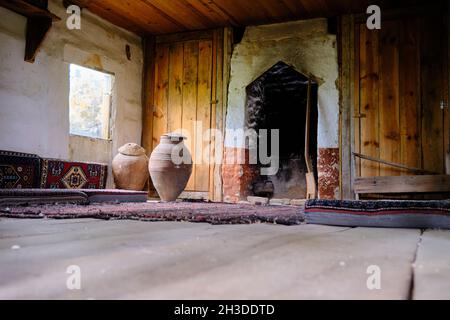 In dem alten und verlassenen Dorfhaus aus Holzmaterial und es gibt große Steingutgläser in der Nähe des Fensters und Teppiche im antiken Stil Stockfoto