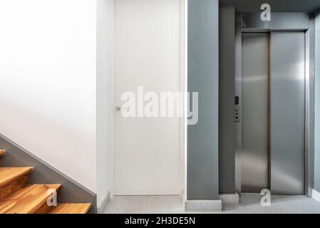 Vorderansicht des Aufzugs mit Edelstahltüren und Treppe mit Kiefernholztreppen Stockfoto