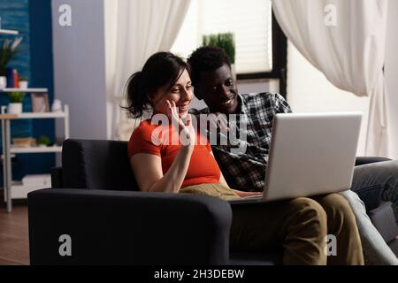 Interracial paar mit Videoanruf Kommunikation auf Laptop zu Hause. Menschen mit gemischter Rasse winken vor der Kamera, während sie auf einer Online-Fernkonferenz über eine Internetverbindung mit Freunden sprechen Stockfoto