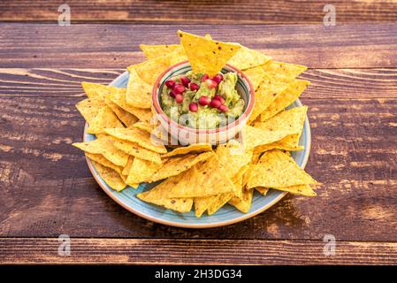 Traditionelle mexikanische Guacamole aus Avocado, Zitrone, Tomate, Zwiebel, Koriander und Chili, gekrönt mit Granatapfelkernen und umgeben von Maissplittern Stockfoto