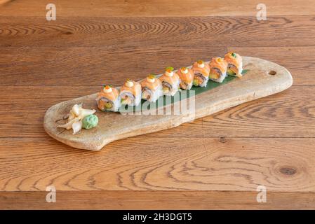 Uramaki Sushi gefüllt mit Lachs mit Avocado, Nori-Algen und bedeckt mit norwegischem Lachs auf japanischem Reis und Bananenblatt mit Wasabi mit Ginseng Stockfoto