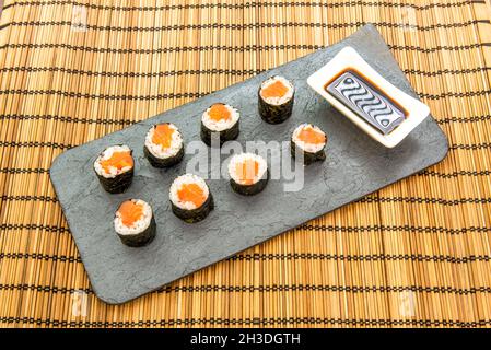 Norwegischer Lachs-Sushi-Maki-Rolle mit weißem Reis und japanischem Essig, gerollt in Nori-Algen mit Sojasauce und Ginseng mit Wasabi auf einem Bambustablec Stockfoto