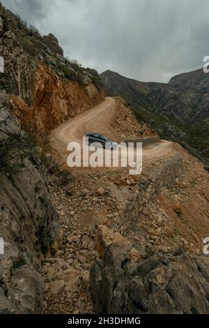 Modernes 4x4-Fahrzeug, das eine steile Schotterpipe durch einen Pass zwischen Bergen abfährt Stockfoto