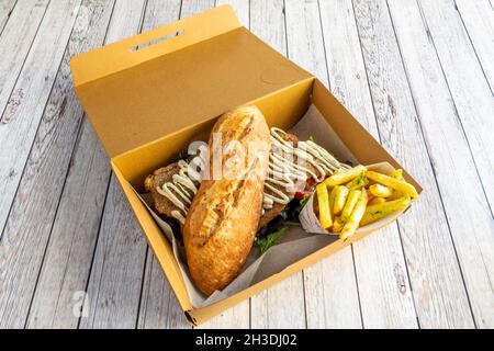 Köstliche Speisekarte mit argentinischem Milanga-Rindfleisch-Sandwich mit Salat und Tomaten, Mayonnaise-Sauce und Pommes Frites im Pappkarton zum Mitnehmen Stockfoto