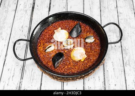 Köstliche spanische Paella mit Meeresfrüchten, galizischen Muscheln, galizischen Jakobsmuscheln und Herzmuscheln über der schwarzen Paella-Pfanne Stockfoto