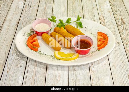 Tablett mit geschmorten und gebratenen Käsestäbchen, Tomaten, Petersilie, Tomatensauce und Joghurtsauce Stockfoto