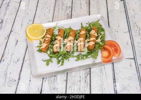 Vorspeise von Mozzarella-Sticks in Weizenmehl, Paniermehl und Ei auf einem Bett von Rucola mit Sauce und Tomate zerschlagen Stockfoto