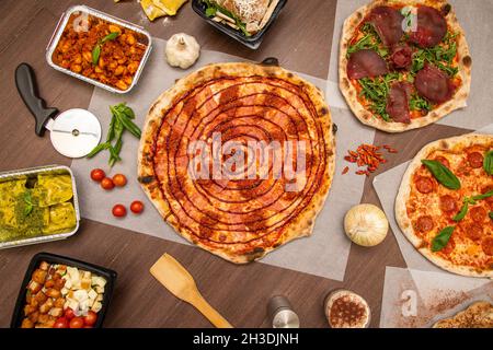 Set von Tellern mit italienischen Speisen, Pasta, Gnocchi und Pizza. Schöne Pizza mit Grillsauce, Salami, geräuchertem Speck, Kirschtomaten, Knoblauch, Pizza schneiden, rav Stockfoto