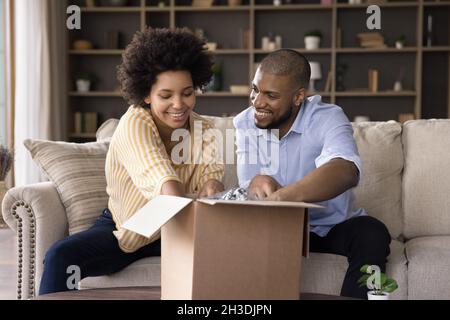 Glückliches afroamerikanisches Paar, das Paket zu Hause auspackt. Stockfoto