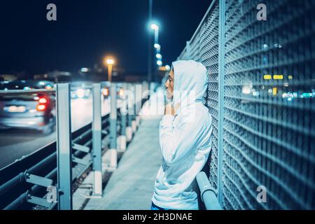 Ein junger Teenager im urbanen Stil mit weißem Pullover, der die vorbeifahrenden Autos sieht und wegfährt Stockfoto