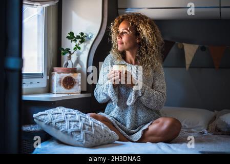 Junge Erwachsene Frau sitzt im Wohnmobil Blick vor dem Fenster am Morgen Frühstück trinken Kaffee und genießen Reisen und Vanlife Lebensstil Stockfoto