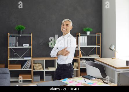 Glücklicher, selbstbewusster, erfolgreicher Geschäftsmann, der am Schreibtisch steht und lächelt Stockfoto