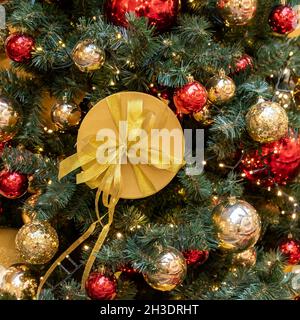 Weihnachten und Neujahr Hintergrund. Weihnachtsbaum mit Girlanden, goldenen und roten Kugeln und geschenkbox in Goldfarbe. Stockfoto