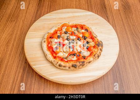 Kleine Pizza mit geschmolzenem Mozzarella-Käse mit Streifen gerösteter roter Paprika, Hühnerstücken, Pilzen und Scheiben schwarzer Oliven mit gerösteter Kirsche Stockfoto
