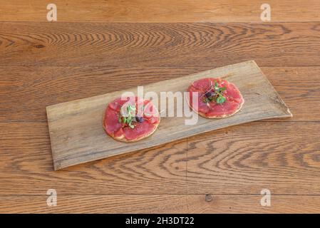 Mini-Pizza mit einer Scheibe rohem rotem Thunfisch und frischem Gemüsesprossen bedeckt Stockfoto