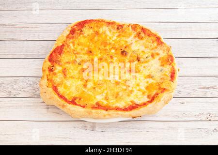 Kleine Pizza mit vier geschmolzenen Käsesorten und Tomaten auf weißem Holztisch Stockfoto