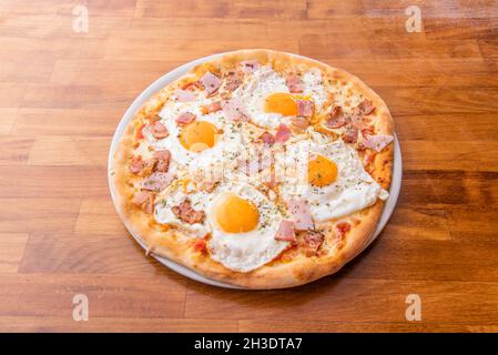 Pizza mit vier Spiegeleiern mit gelbem Eigelb zum Eintauchen von Brot mit Schinkenstücken und Huhn mit Orangano Stockfoto