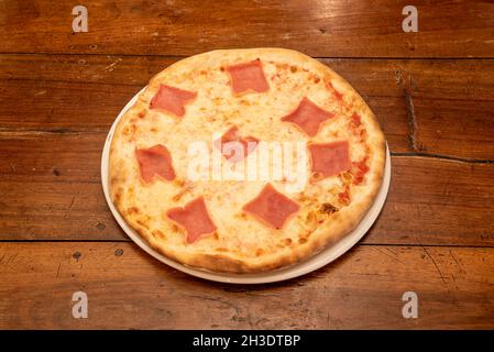 Italienische Mozzarella-Käse-Pizza mit Stücken gekochten Schinkens auf einem Holztisch Stockfoto