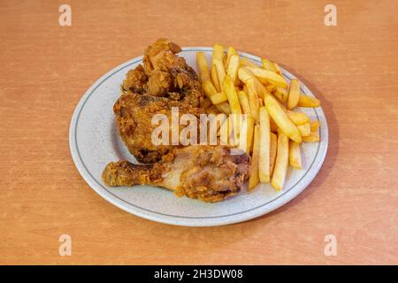 Portion Brathähnchen im Teig in Olivenöl gebraten, garniert mit Pommes auf Holztisch Stockfoto