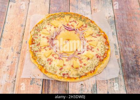 Tropische Pizza mit einer Scheibe Ananas und Scheiben um sie herum mit roten Zwiebeln, Stücken geräuchertem Speck und Mozzarella-Käse mit viel Oregano Stockfoto