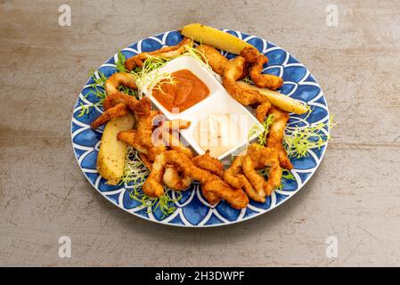 Hähnchenstreifen im Teig und gebraten mit Kartoffelkeilen mit eintauchenden Saucen Stockfoto