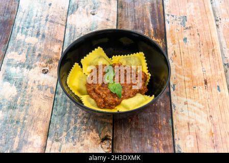 Köstliche, mit Fleisch gefüllte Ravioli mit Bolognese-Sauce und Basilikumblättern darauf Stockfoto